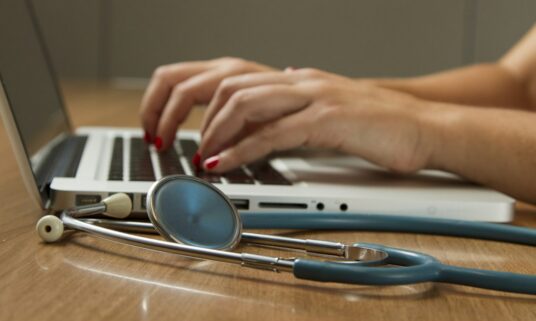 Hands typing on a laptop beside a stethoscope while updating provider data
