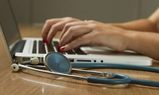 Hands typing on a laptop beside a stethoscope while updating provider data