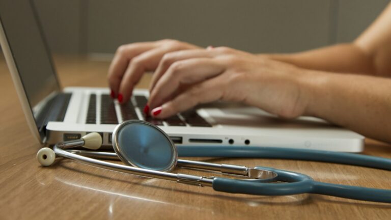 Hands typing on a laptop beside a stethoscope while updating provider data