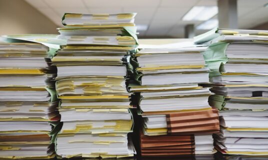 Stacks of provider credentialing files awaiting primary source verification