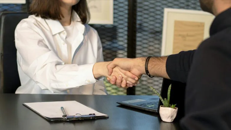 Employer and employee shaking hands across a desk over benefits paperwork